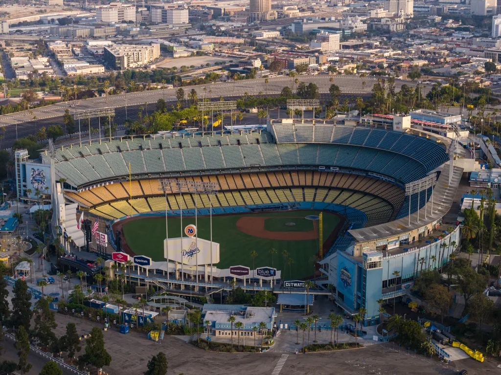 Aerial view of Dodger Stadium in Los Angeles, California, surrounded by palm trees and city buildings.