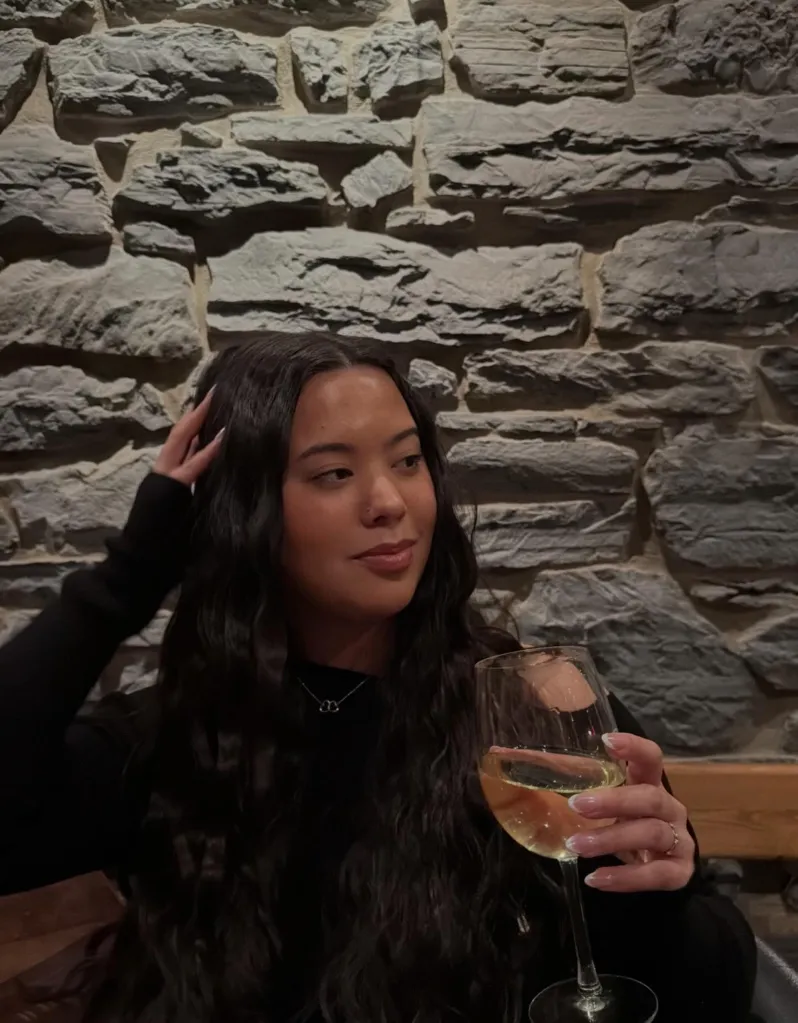 Hannah Gosselin sitting in front of a stone wall holding a glass of wine.