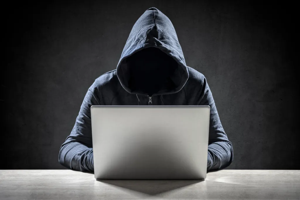 Illustration of a hooded computer hacker typing on a laptop.