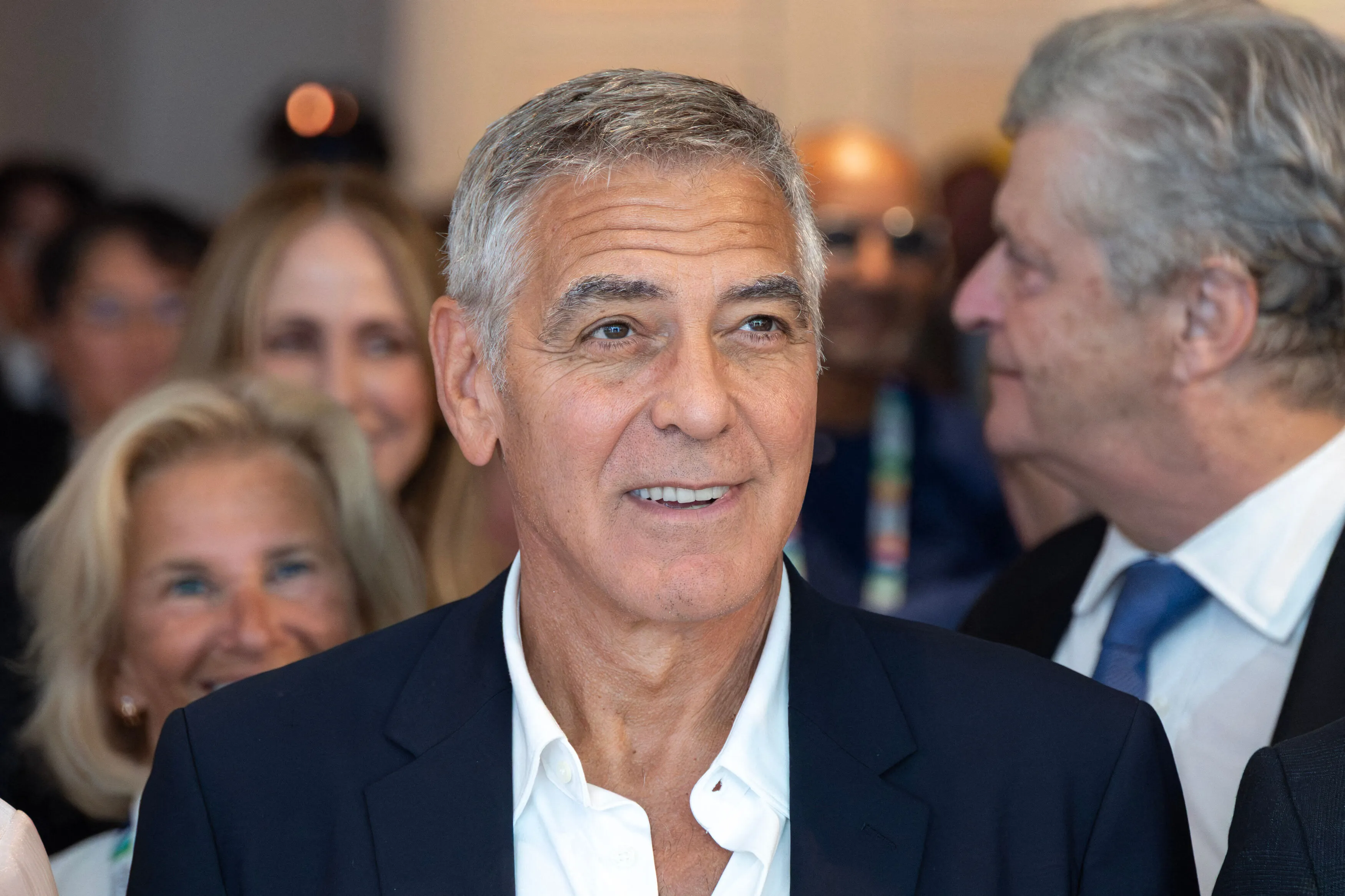 George Clooney smiling in a crowd of people.