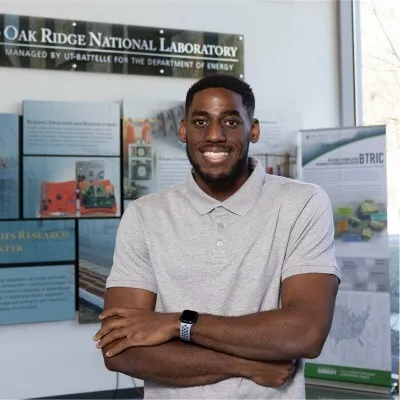 Stanford PhD student Obi Nnorom stands in front of a sign for Oak Ridge National Laboratory.