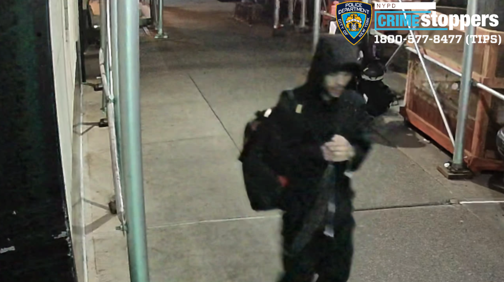Surveillance camera image of a man wanted by NYPD Crime Stoppers walking down a city sidewalk.