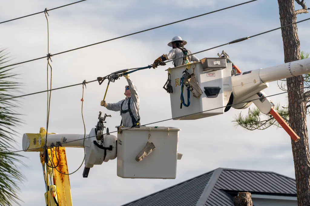 Utility crews work in bucket trucks to repair power lines damaged by a hurricane.