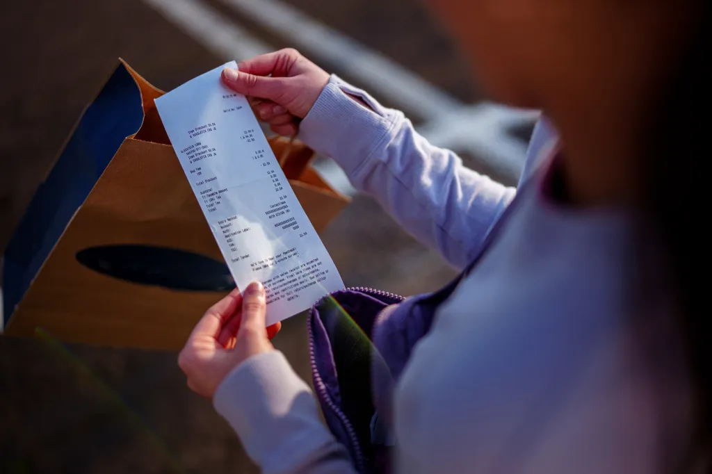 A teenage girl checks a receipt in the parking lot of a strip mall.