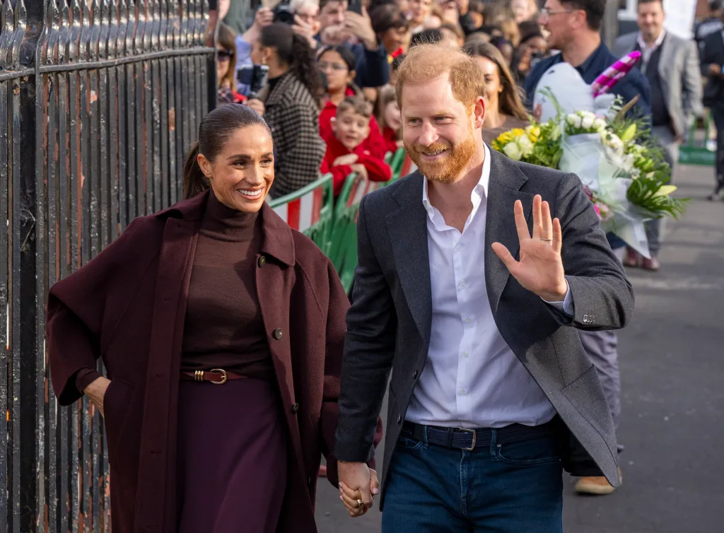 Prince Harry, in a grey blazer and white shirt and jeans, and Meghan Markle, in a burgundy coat, burgundy turtleneck and burgundy pants, wave to well-wishers during a visit to Nottingham.