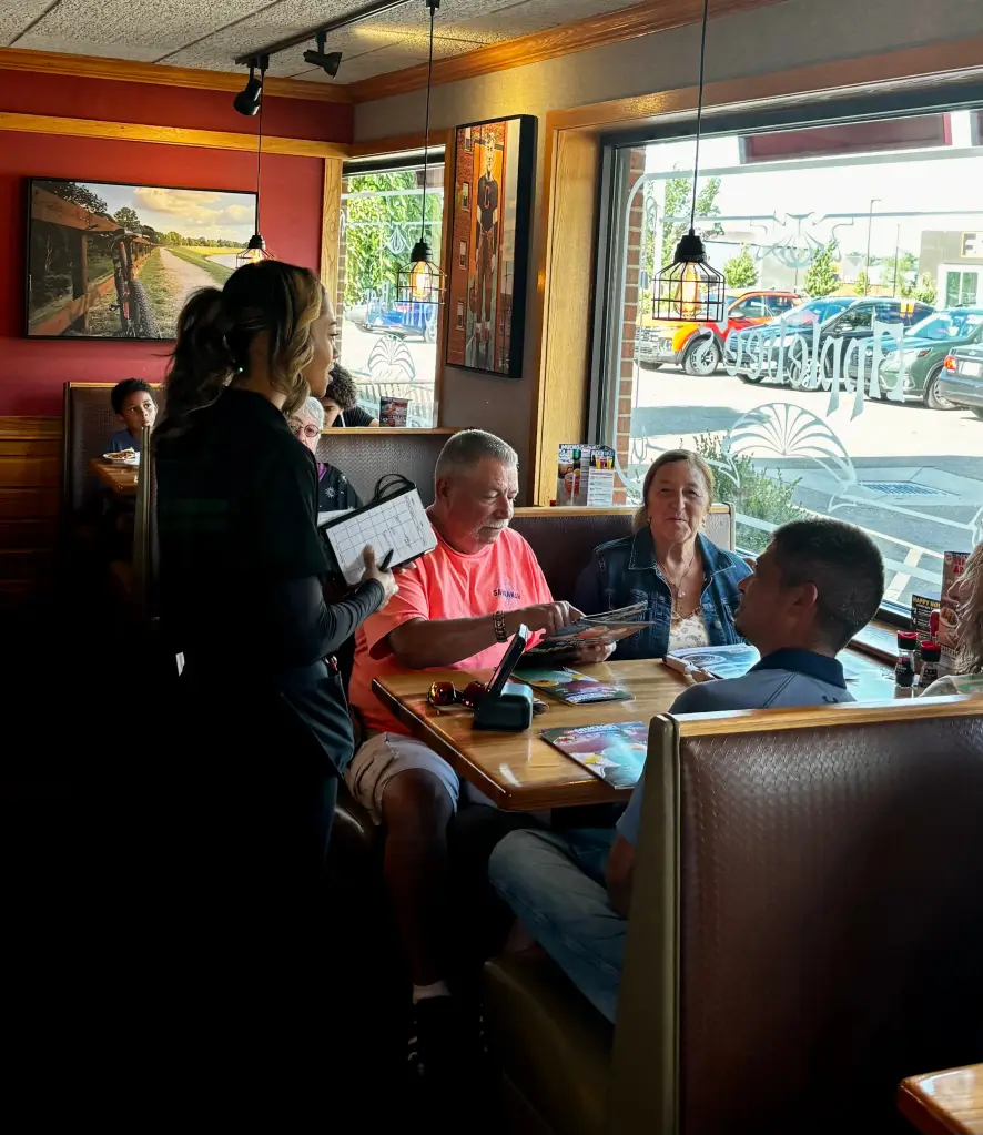 A server takes an order from customers in a busy Applebee's restaurant booth.
