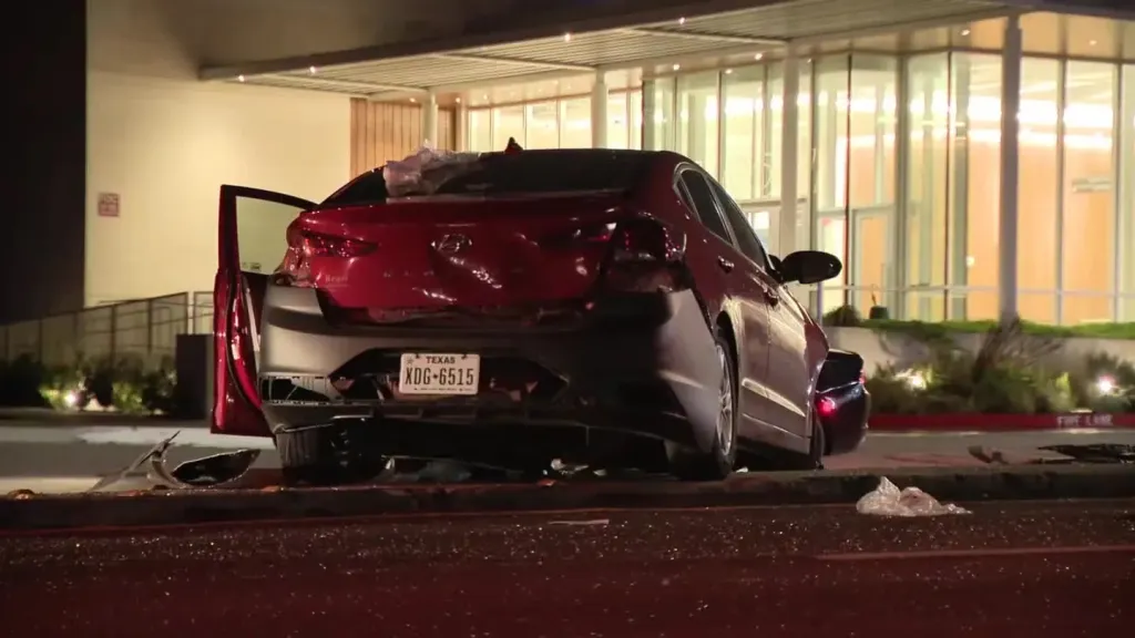 A damaged red Hyundai parked on the street at night with its rear end heavily dented.