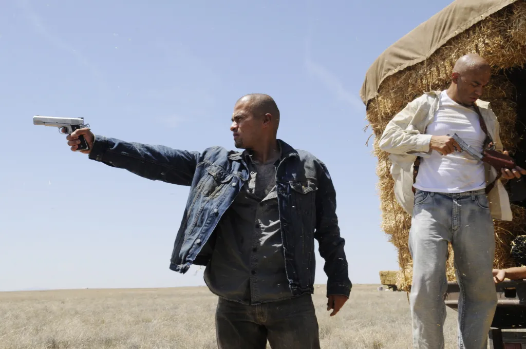 Daniel and Luis Moncada as the Cousins in Breaking Bad, standing in a field with a hay cart and holding guns.