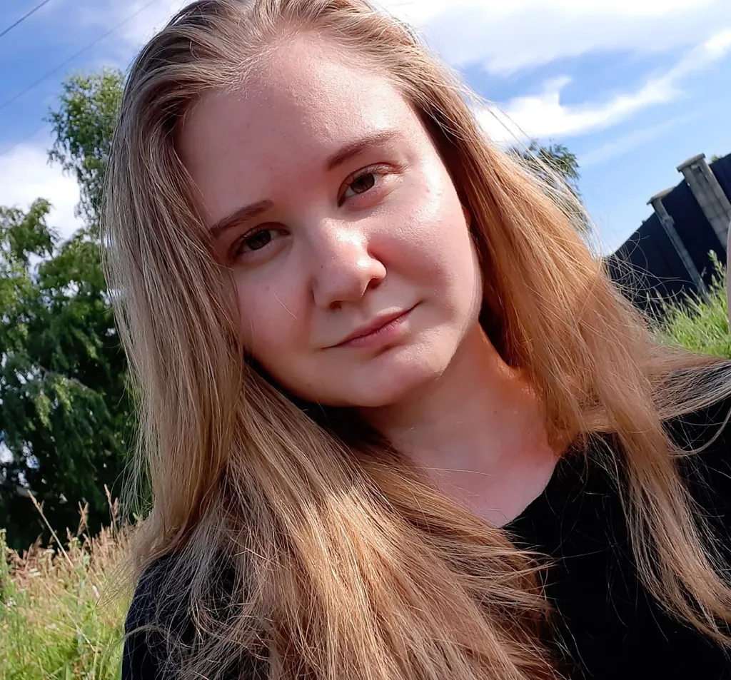 Daria Shipilova outdoors against a backdrop of trees and a blue sky.
