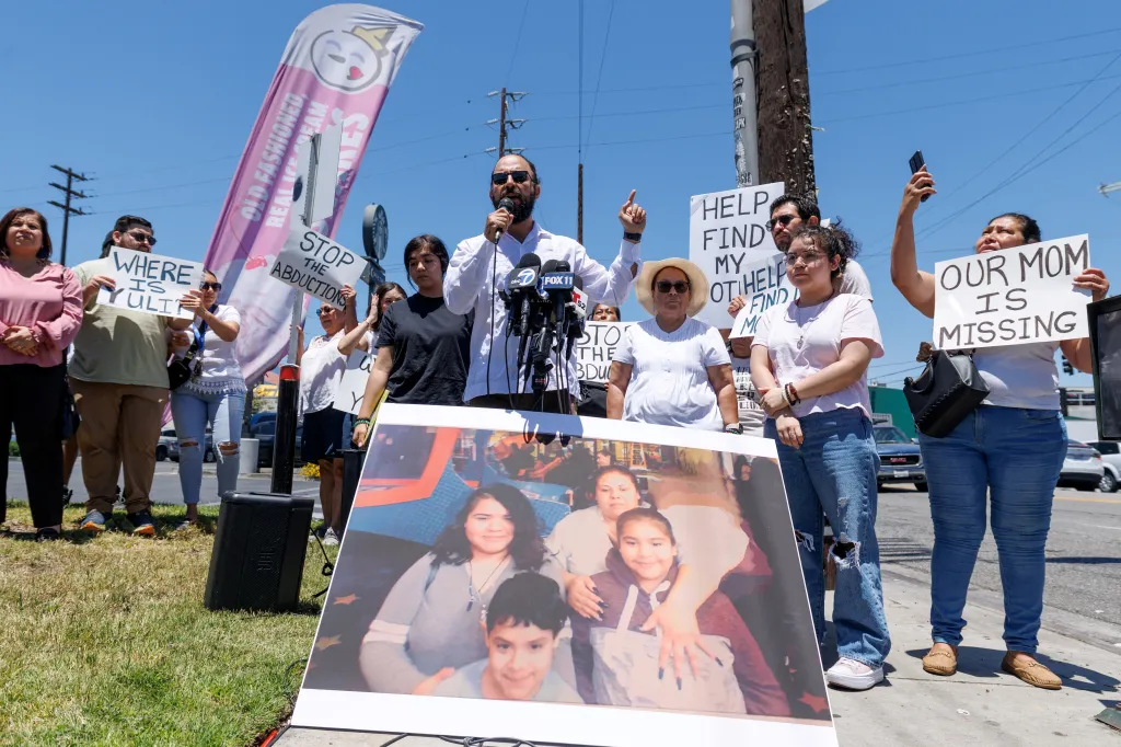 A lawyer speaks at a press conference next to a picture of a missing woman, surrounded by family and community members holding signs that read