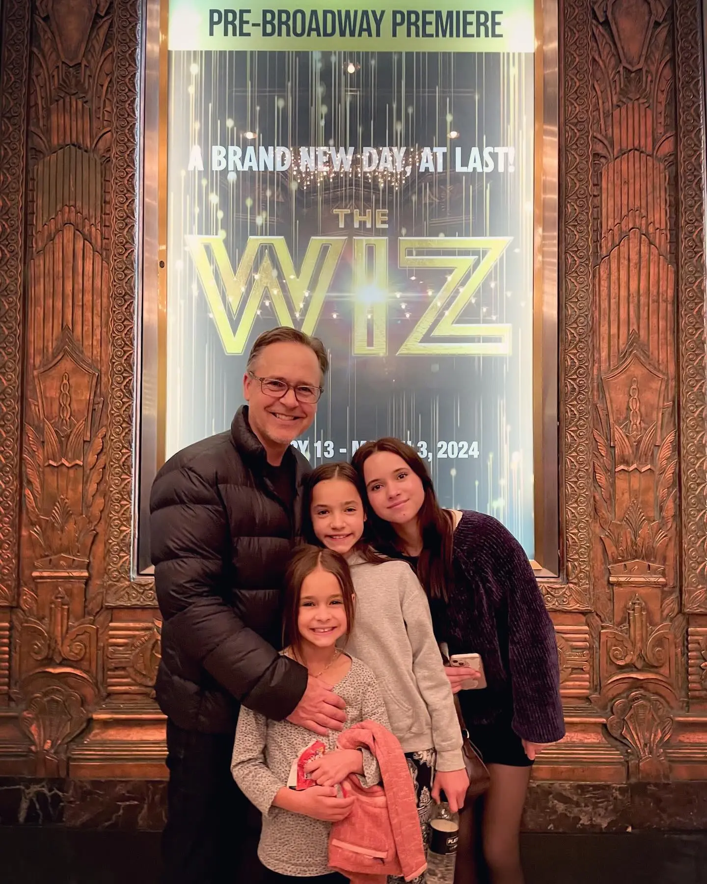 Chad Lowe and his daughters Mabel, Fiona, and Nixie pose in front of a poster for The Wiz.