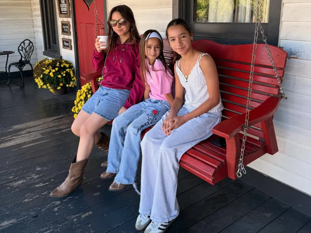 Chad Lowe's daughters Mabel, Fiona, and Nixie sitting together on a red porch swing.