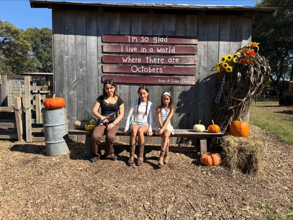 Chad Lowe's daughters Mabel, Fiona, and Nixie sit on a bench outside a rustic wooden building with a sign that reads,