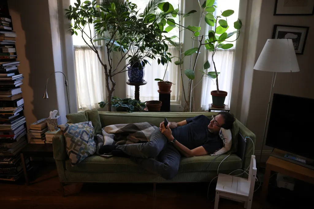 David Sabatini lies on a green sofa, using a smartphone in his living room filled with plants.