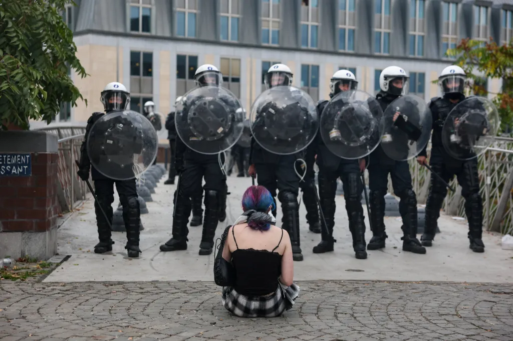 A demonstrator sits on the ground in front of a line of police officers in riot gear during a protest in Liege.
