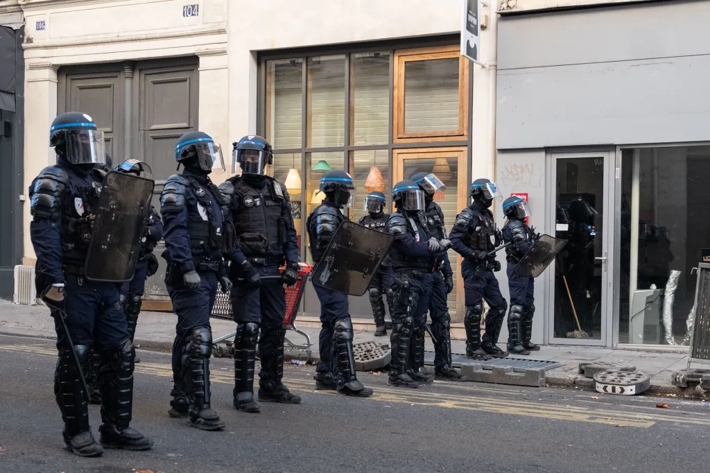 French riot police in full protective gear stand in a street in Paris.