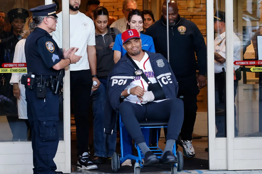 Detective Jose Mercedes in a wheelchair, leaving the hospital, surrounded by police officers and supporters.