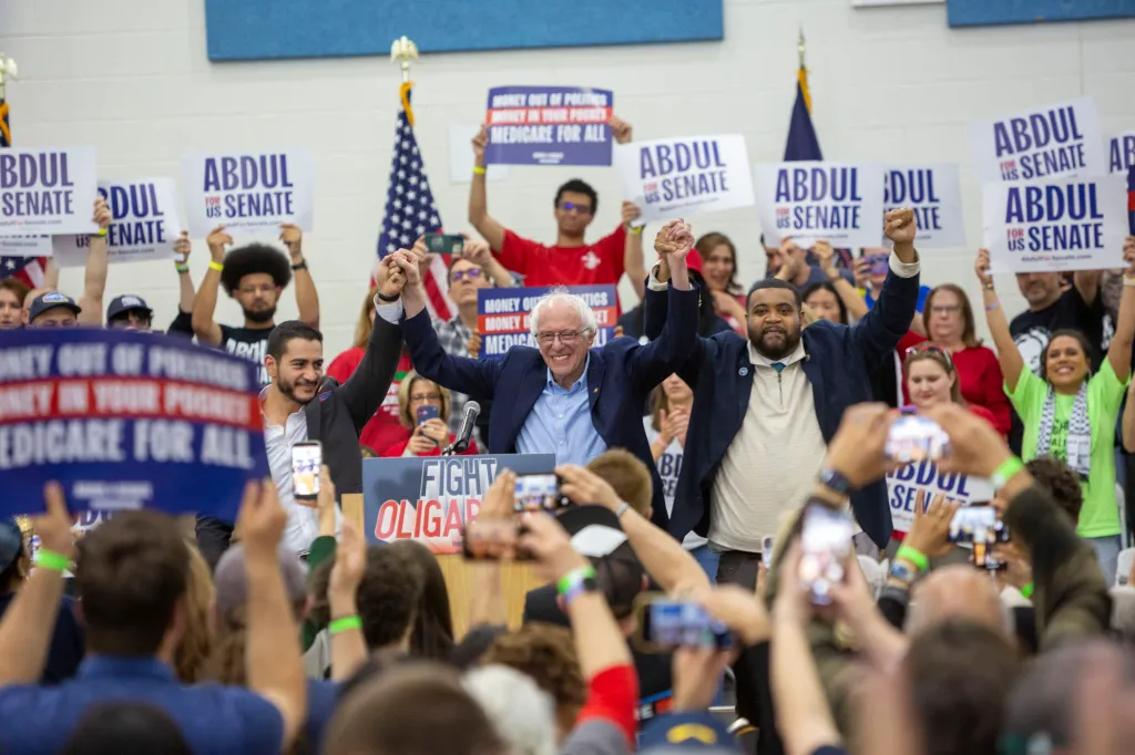 Sen. Bernie Sanders holds up the hands of Dr. Abdul El-Sayed and Donavan McKinney at a rally.