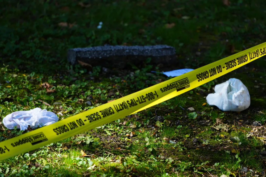 A diaper and a baby onesie lie on the ground near a crime scene tape.