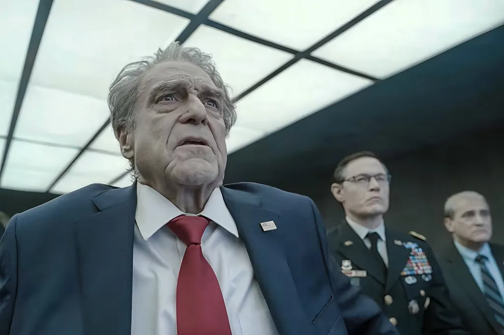 John Goodman in a suit and red tie looking up with two other men in the background.