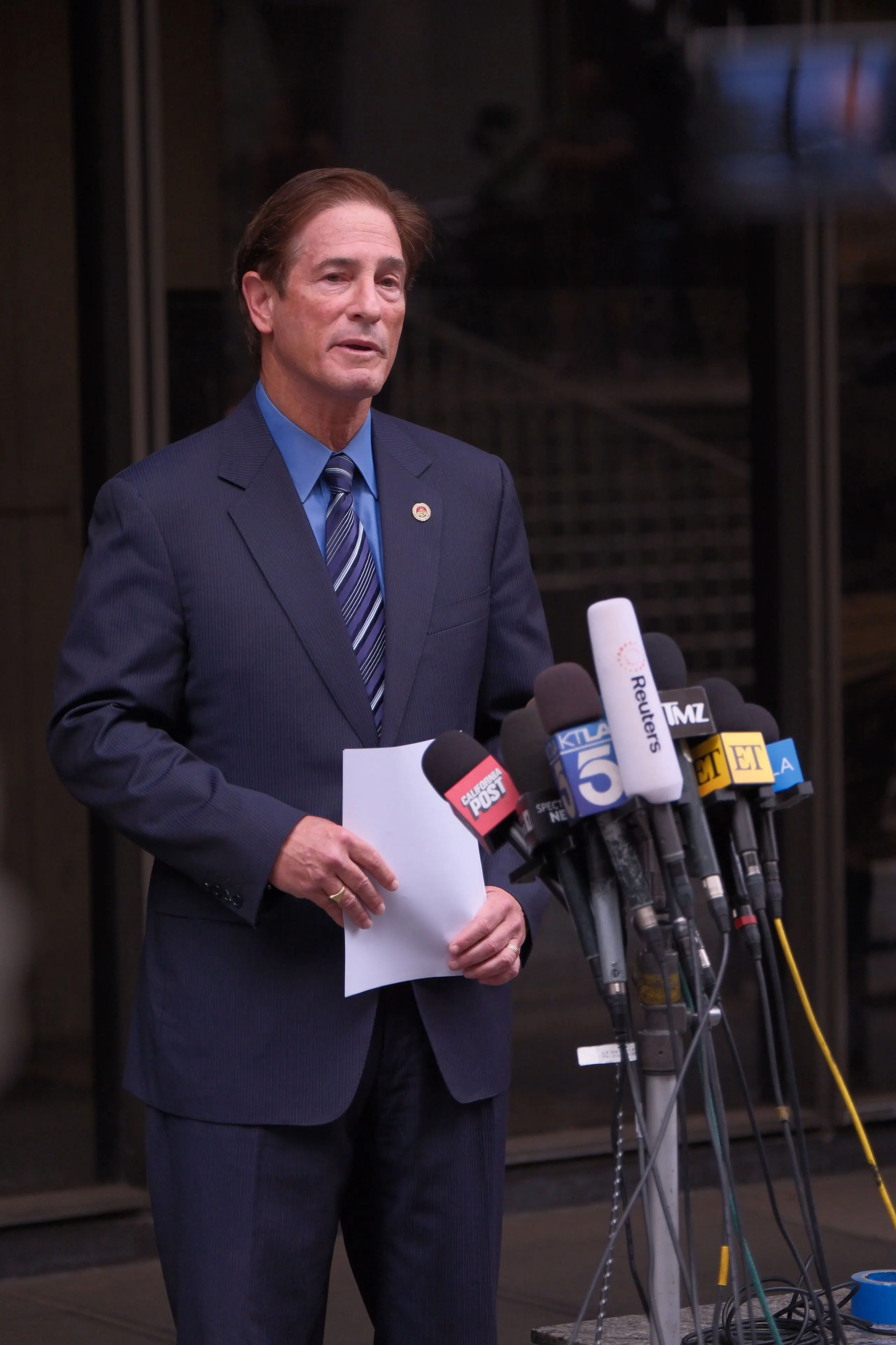 District Attorney Hochman speaking at a podium with news microphones.