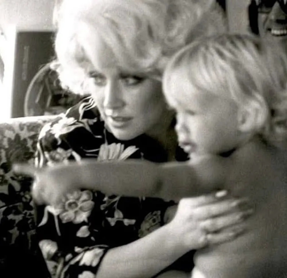Dolly Parton holding a young child who is pointing forward.