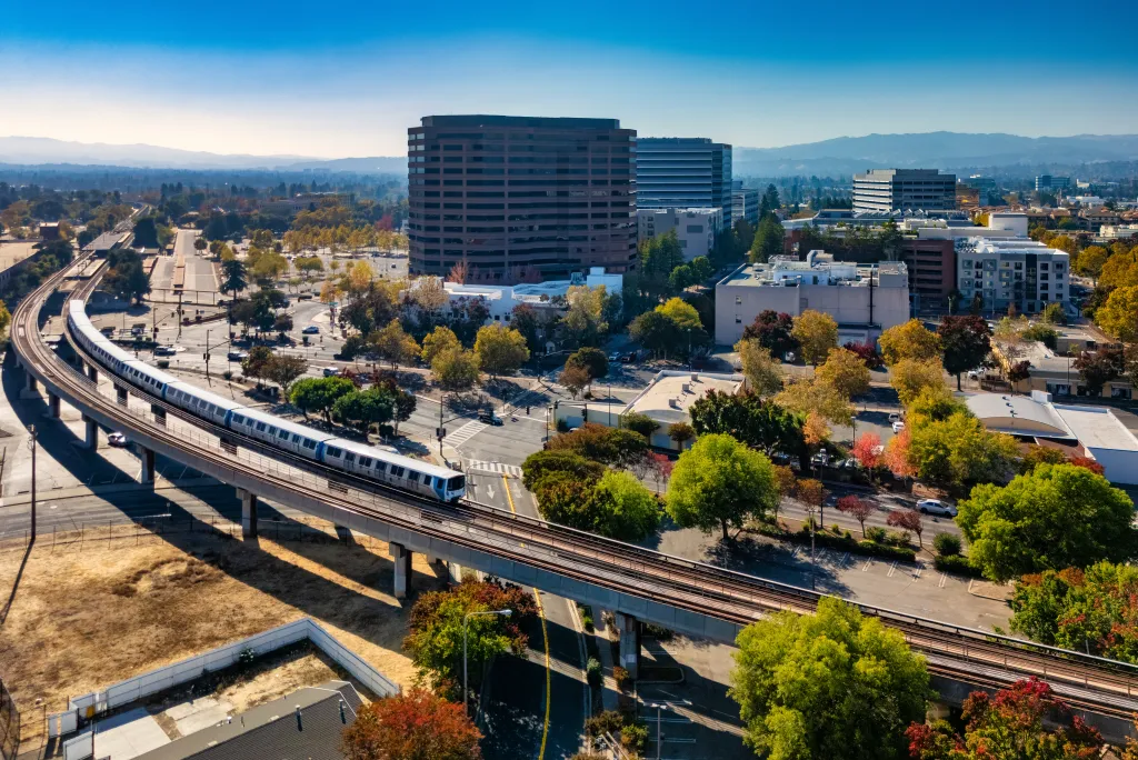 A BART train travels on elevated tracks in the foreground, with the Downtown Concord skyline and Diablo Range mountains in the background.