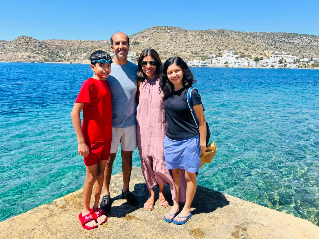 Dr. Rachna Shroff standing with her family on a stone pier by the blue sea.