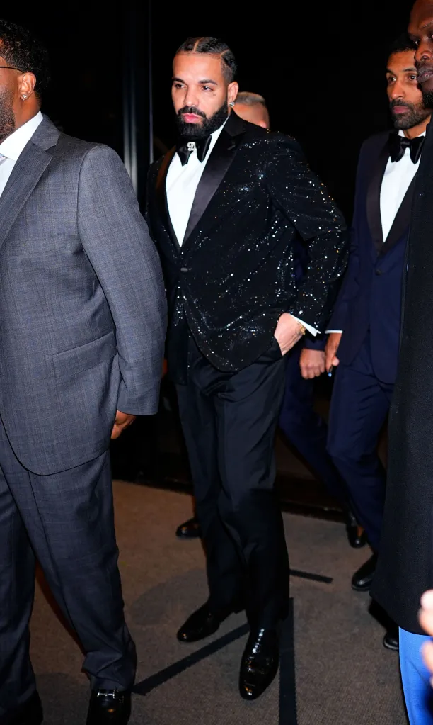 Drake wearing a black sequined tuxedo and bow tie, flanked by bodyguards in New York City.
