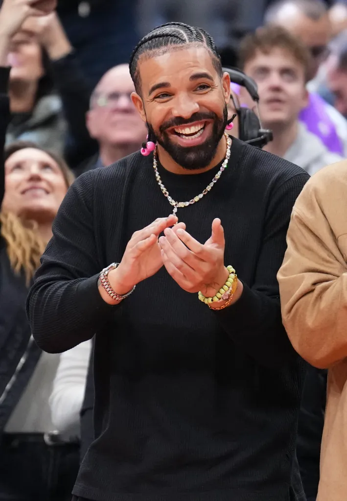 Drake smiling and clapping while attending a Toronto Raptors basketball game.