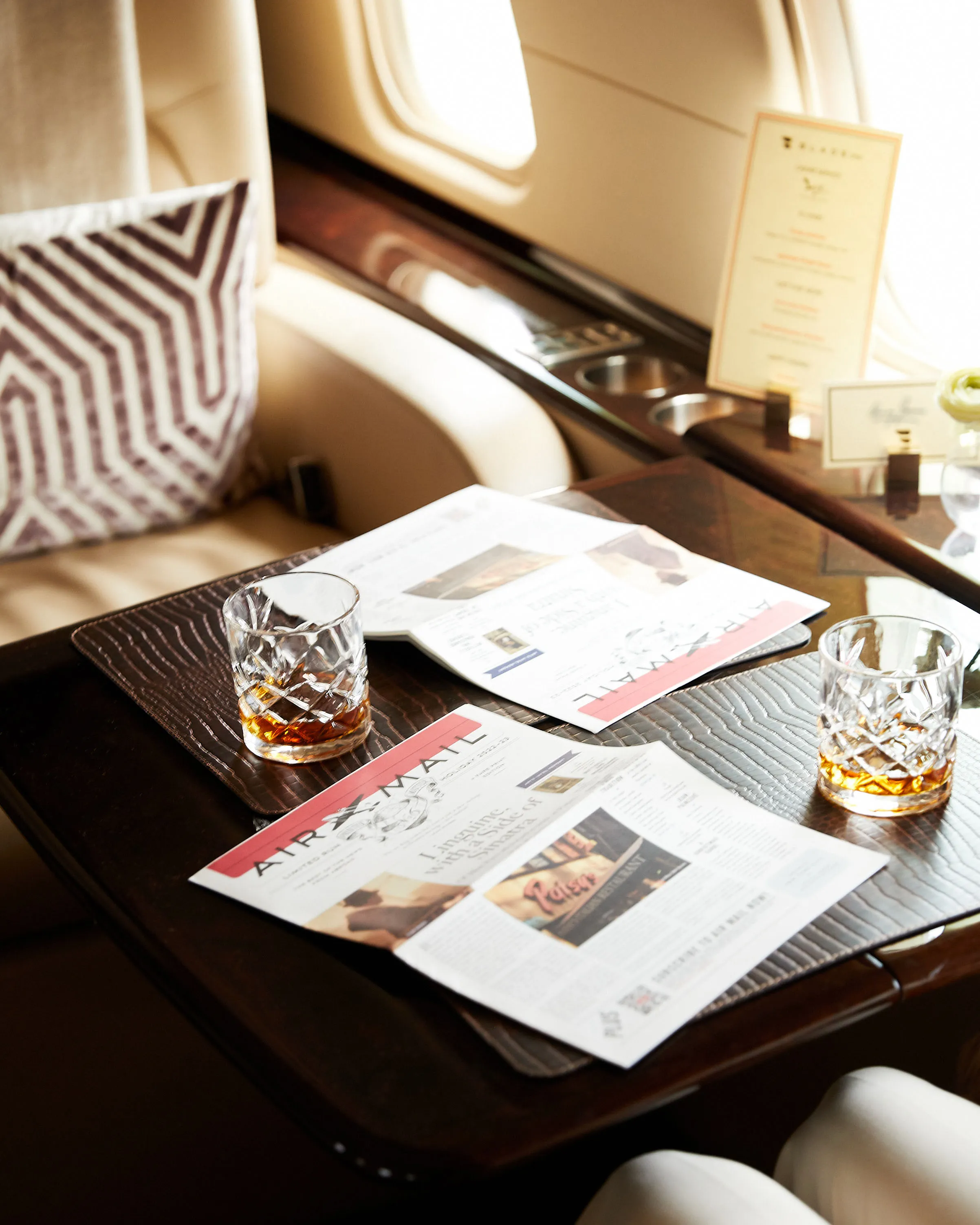 Inside the luxury BLADEone jet, a wooden table holds two glasses of amber liquid and issues of Air Mail.