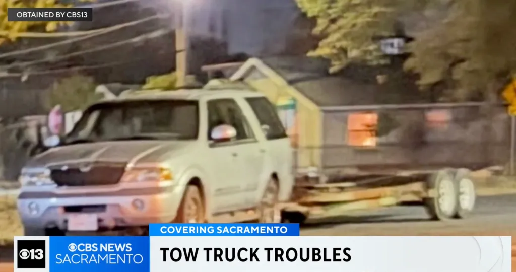 A white SUV towing a trailer on a street at night.