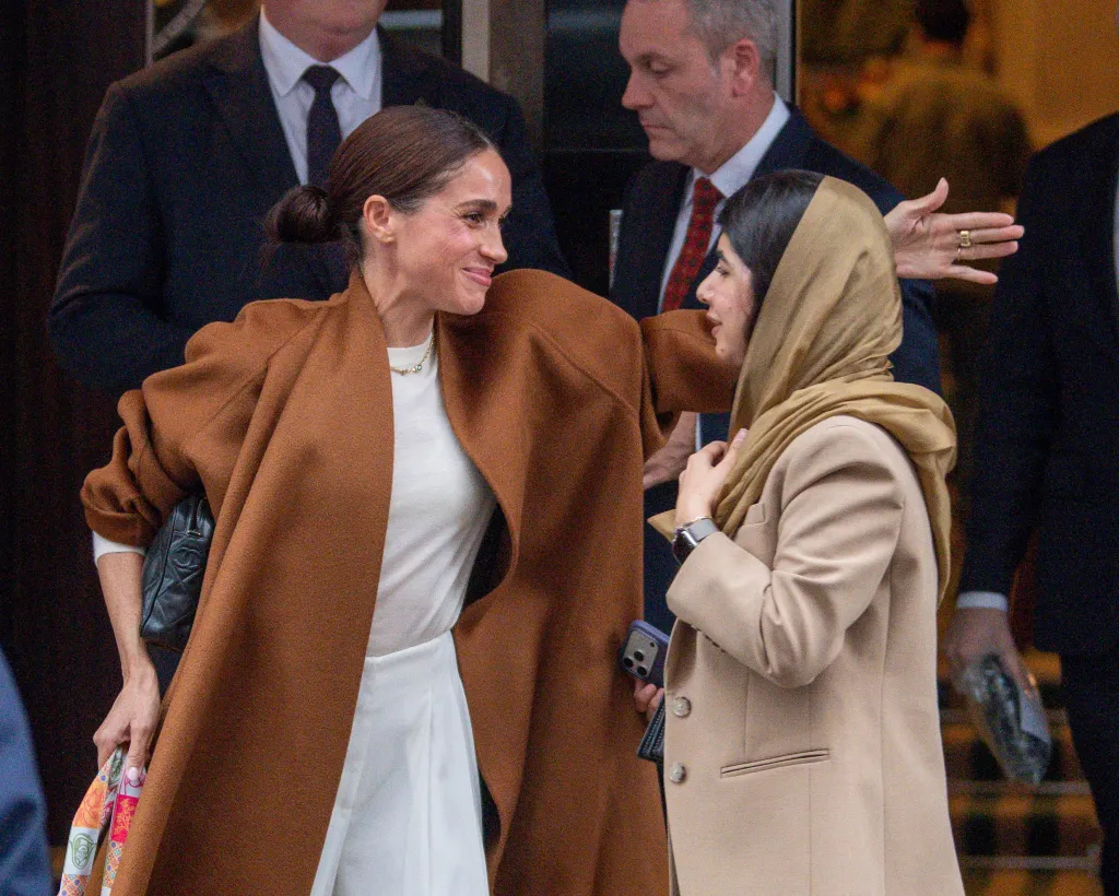 Meghan Markle, in a brown coat, cream top and white pants, and Malala Yousafzai, in a brown jacket, brown headscarf and brown striped pants, eaving Claridge’s hotel in London.