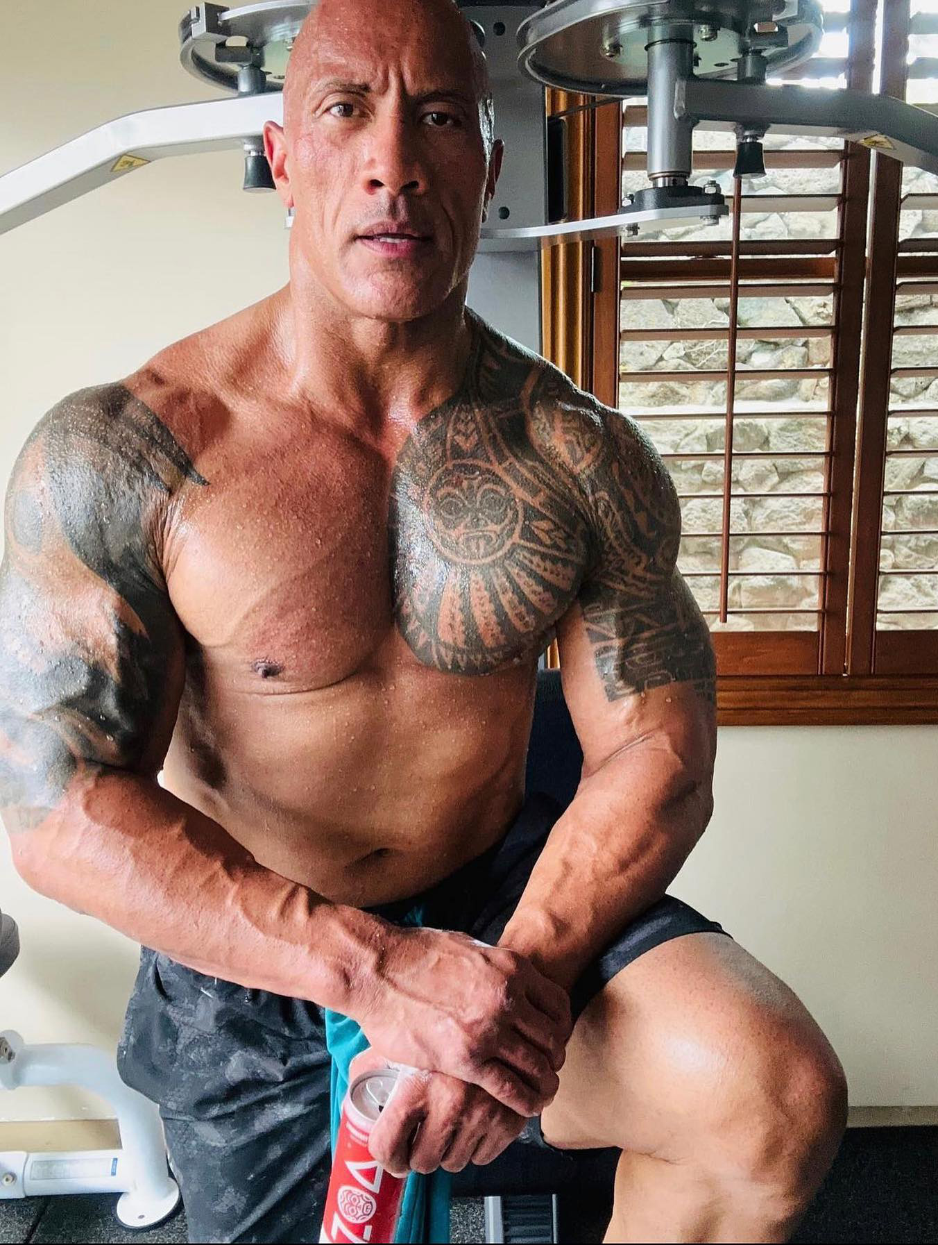 Dwayne Johnson posing in the gym while holding a can of ZOA Energy Drink.
