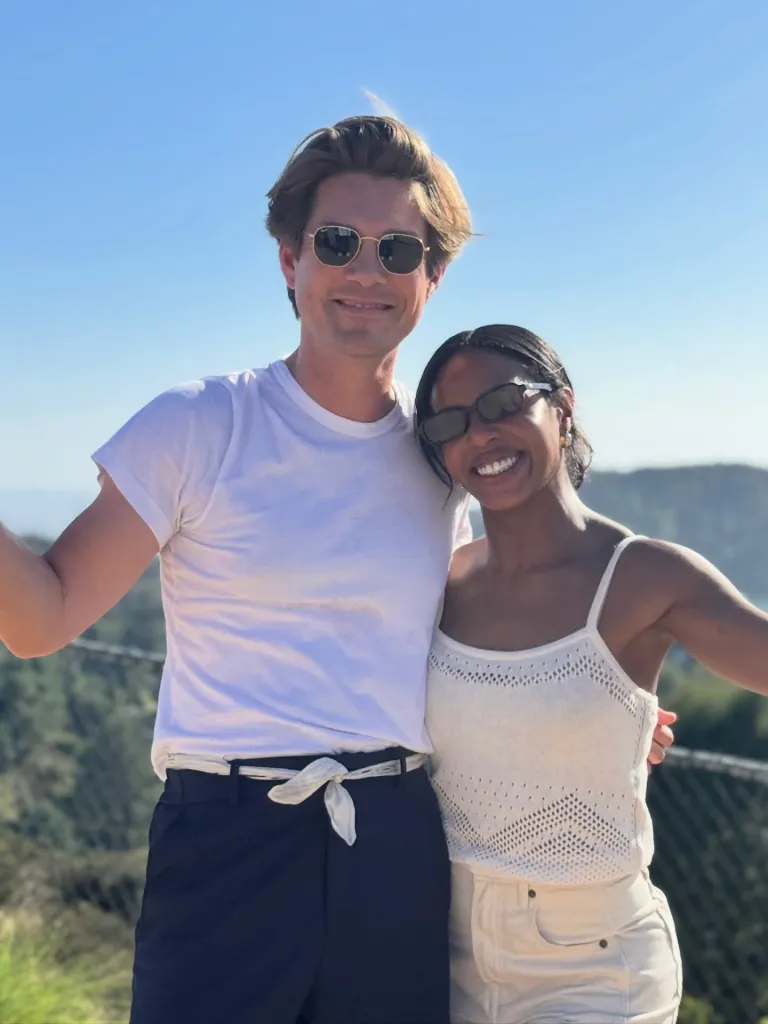 Taylor Hanson and DWTS pro Britt Stewart smiling together outdoors in matching white tops and sunglasses.