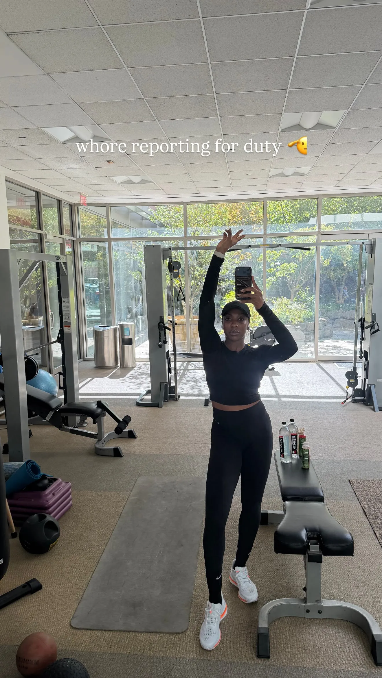 Ego Nwodim takes a mirror selfie in a gym, wearing all-black workout clothes and a cap, with text that reads 