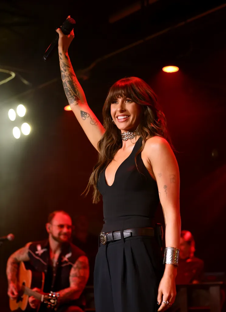 Ella Langley performs live onstage, holding a microphone aloft with one arm.