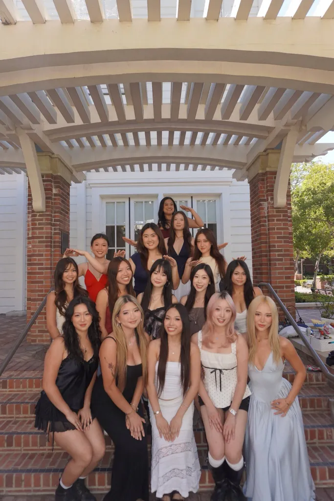 Elsa Cai posing with a group of young women outdoors on brick steps beneath a pergola.