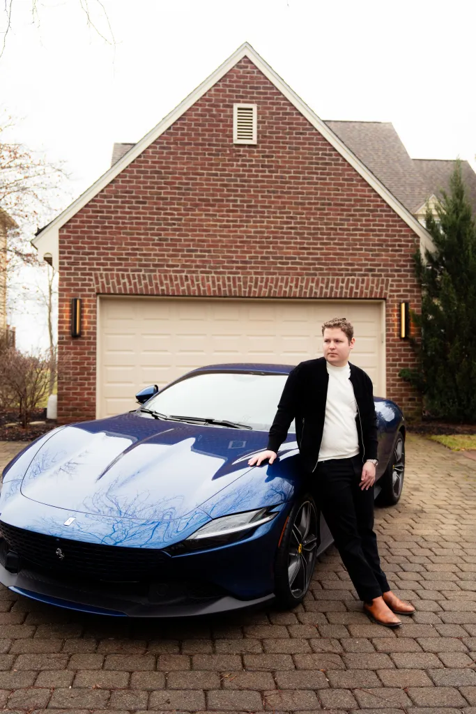 Emil Barr, founder of Flashpass, leans against a blue sports car in front of a brick house.