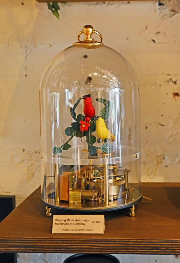 Two singing birds automaton in a glass bell jar on display with a price tag in front.