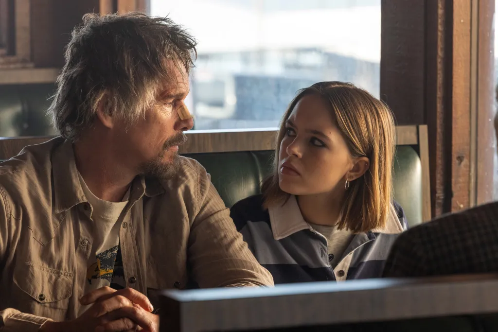 Ethan Hawke and Ryan Kiera Armstrong seated in a booth in a scene from
