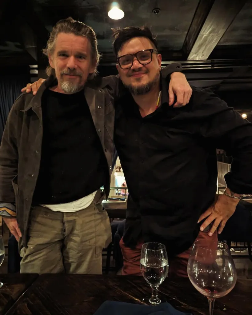Ethan Hawke and Sterlin Harjo pose for a photo with their arms around each other.
