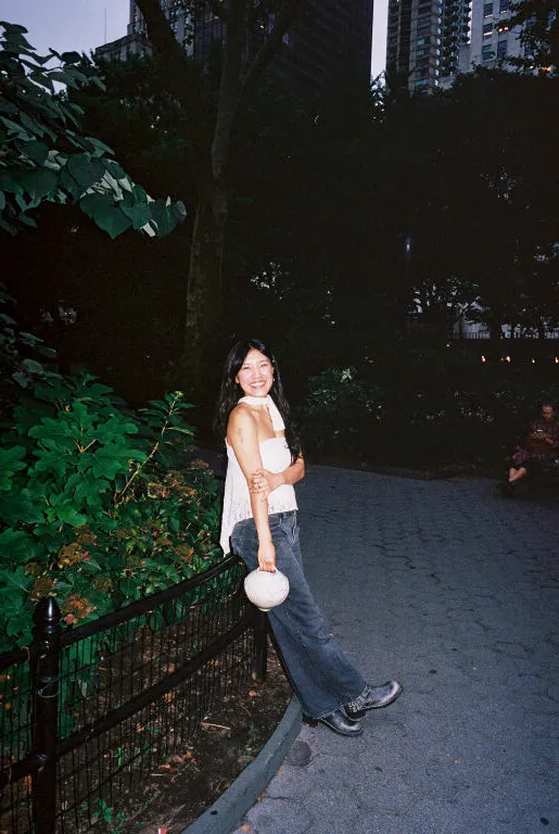 Artist Eujue smiling while leaning against a fence in a New York park.
