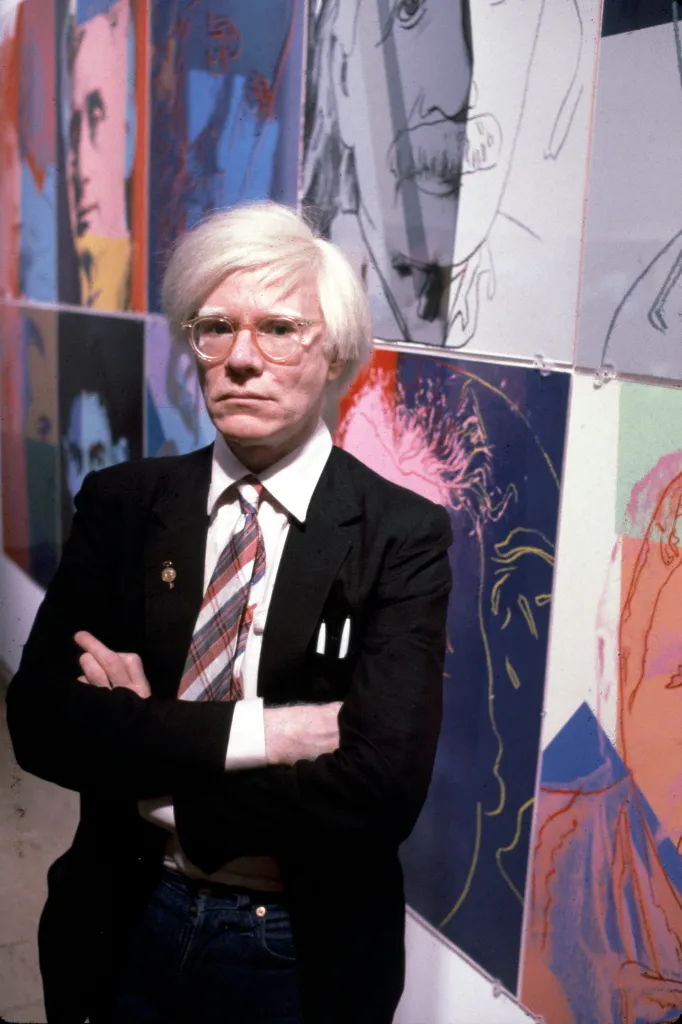 American artist and filmmaker Andy Warhol poses with his paintings.