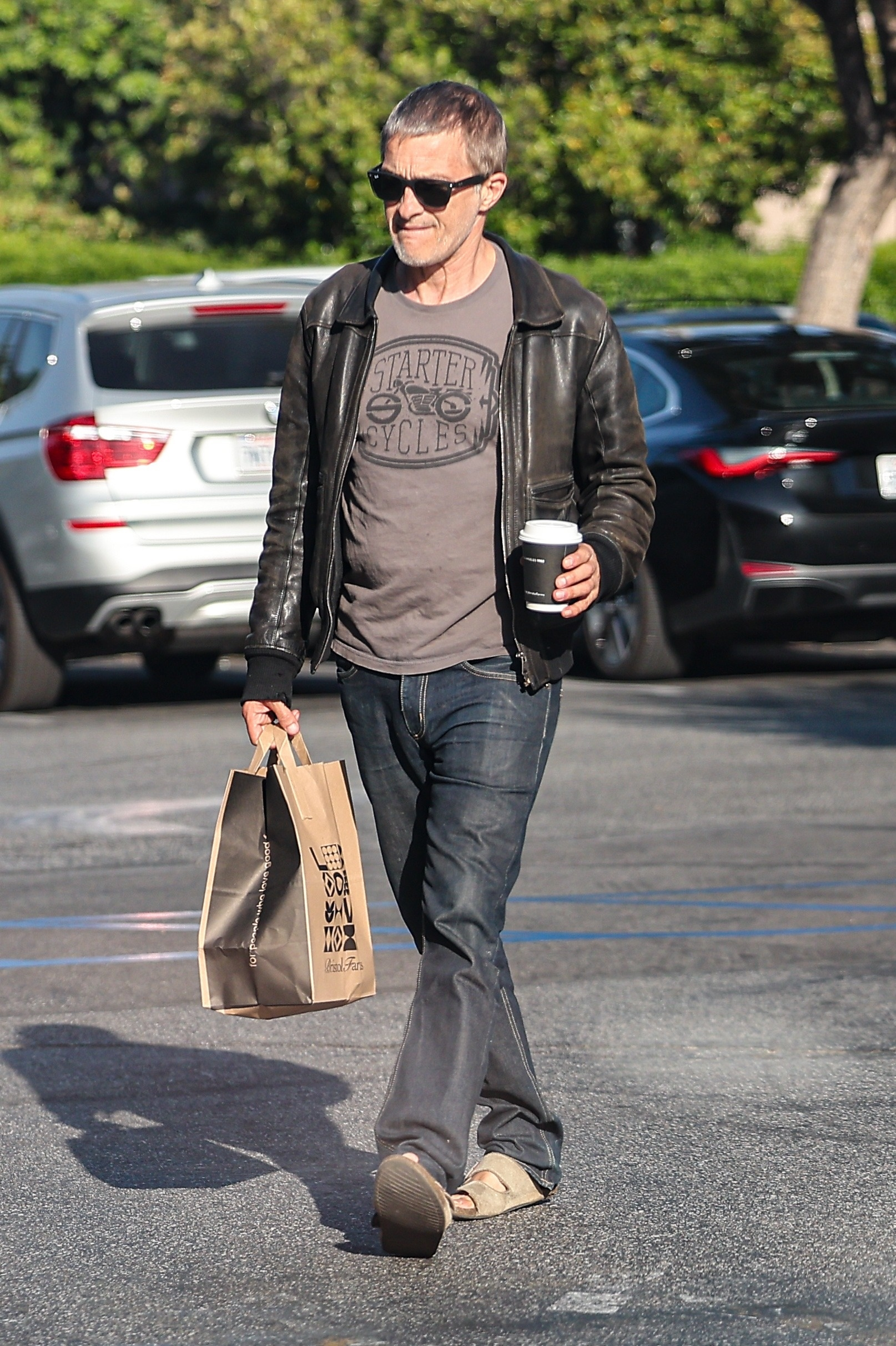Olivier Martinez walking outdoors while carrying shopping bags and coffee.