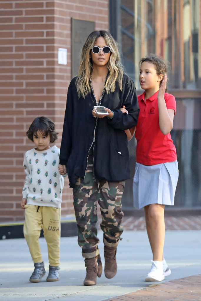 Halle Berry, in sunglasses, a black jacket and khaki pants, walking with her children, Nahla, in a red T-shirt and grey skirt, and Maceo, in a patterned white sweatshirt and yellow shorts.