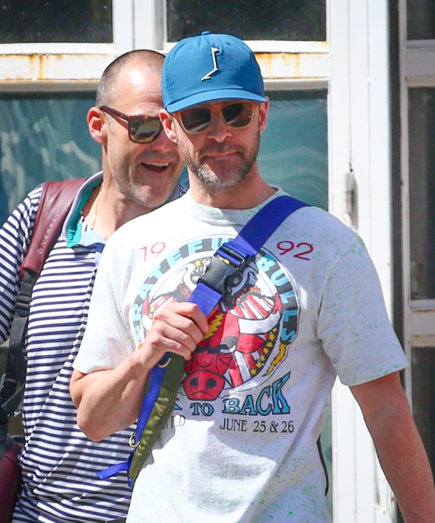 Justin Timberlake wearing a blue baseball cap and sunglasses while walking outside with his bodyguard.