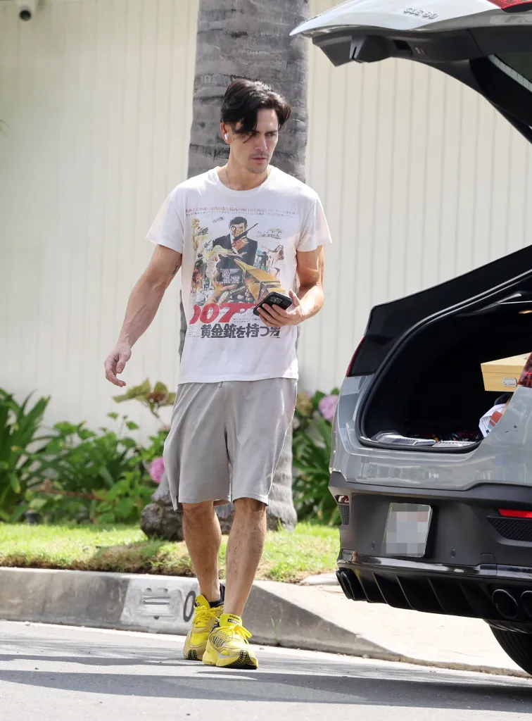 Tom Sandoval walks past the open trunk of a car, holding his phone.