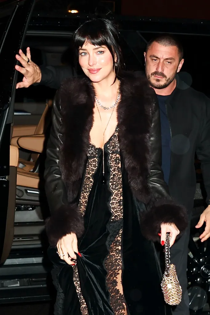 Dakota Johnson wearing a black Stella McCartney dress and fur-trimmed leather coat while arriving at a restaurant in New York City.