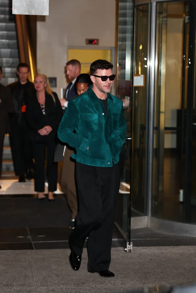 Justin Timberlake in a green jacket and sunglasses walking outside in New York City.